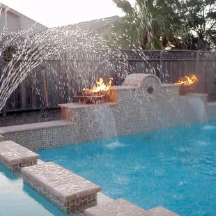 Pool and spa with elevated walls, fountain, and fire bowl accents.