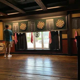 a man standing in front of a bar with darts on the wall