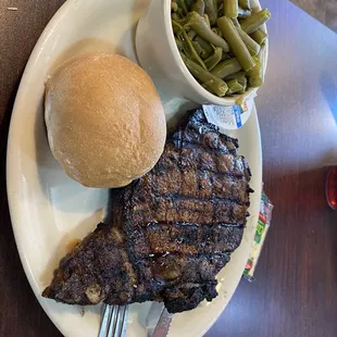 a plate of steak, green beans, and a roll