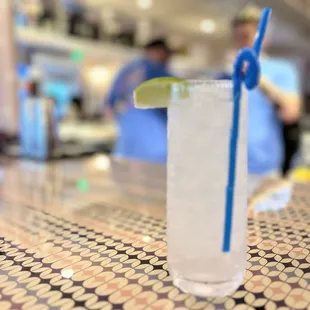 a tall glass with a blue straw and a lime slice
