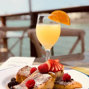 a plate of french toast with fruit and a glass of orange juice