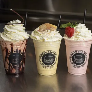 three milkshakes with strawberries and whipped cream