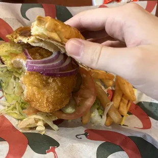 a hand holding a burger and french fries