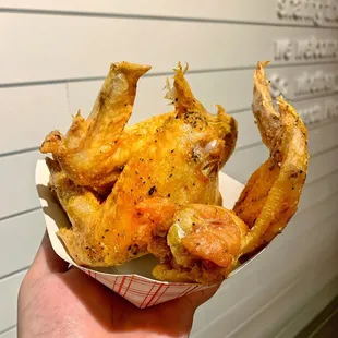 a hand holding a basket of fried chicken