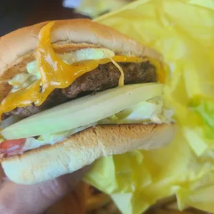 a hand holding a hamburger with lettuce and cheese