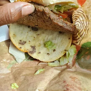 a hand holding a sandwich with meat and lettuce