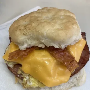 Ham, Bacon, Egg and Cheese Biscuit.   Grilled Ham, Tasty Bacon, A Real Egg covered with cheese on a Buttery Biscuit.