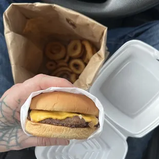 a person holding a hamburger in a styrofoam container
