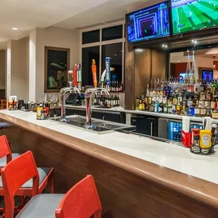 a bar with red chairs and televisions