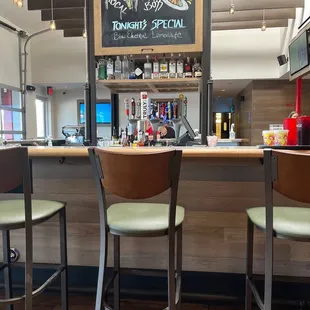 a bar with two stools and a chalk board