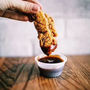 a hand dipping a piece of fried chicken