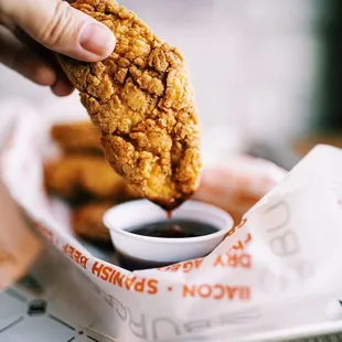 a person dipping a piece of fried chicken