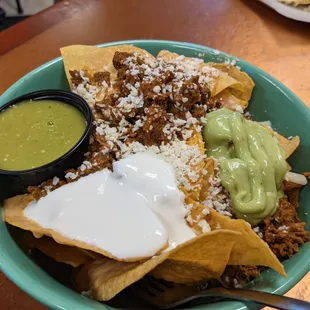 Steak nachos with guacamole and sour cream. Salsa Verde in the cup.