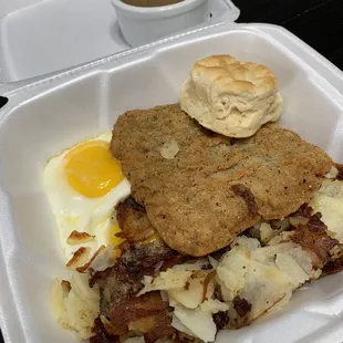 Country Fried Steak with 2 sunny side up eggs, home fries, and a biscuit.  Gravy is on the side.