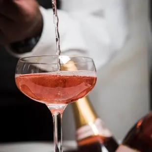 a person pouring a drink into a wine glass