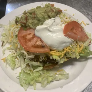 Beef tostada beans beef lettuce cheese guacamole sour cream and tomatoes