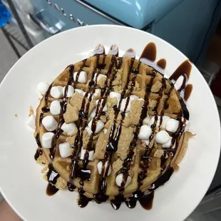 s'mores waffle topped with graham crackers, marshmallows, chocolate chips, and chocolate syrup
