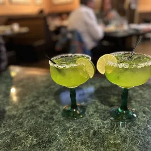 two margarita glasses on a bar