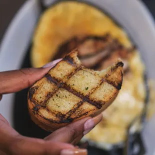 a hand holding a piece of grilled bread