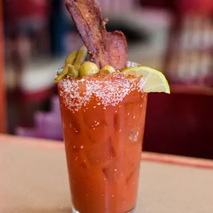 a bloody drink with bacon and a slice of lime