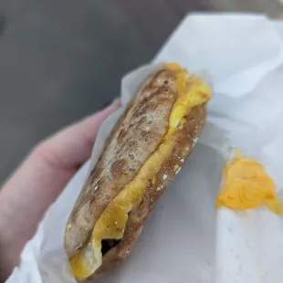 a hand holding a sandwich with cheese and egg