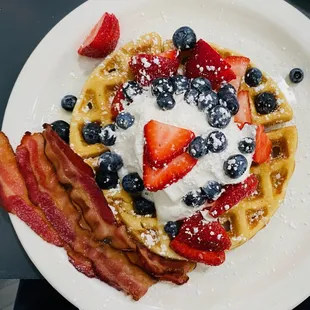 a waffle with strawberries, blueberries, and bacon