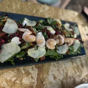 a plate of salad with shrimp and pomegranates
