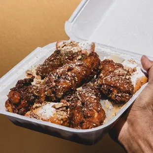 a hand holding a takeout container of chicken wings