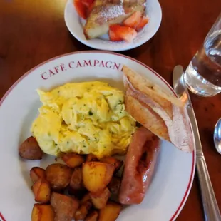 Scramble eggs, potatoes, chicken and pork sausage, and a side of French toast with strawberries coated with powder sugar and cinnamon.