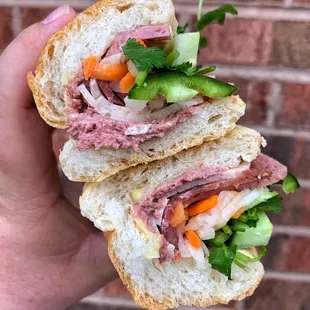 a hand holding a sandwich with meat and vegetables