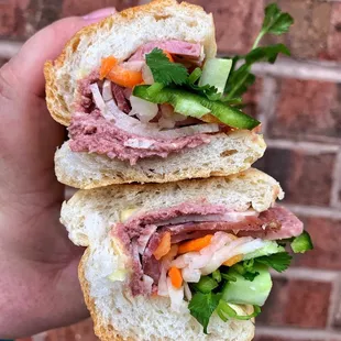 a hand holding a sandwich with meat and vegetables