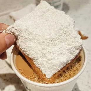 a hand holding a piece of cake in a cup of coffee