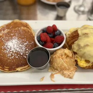 a plate of pancakes, berries, and syrup