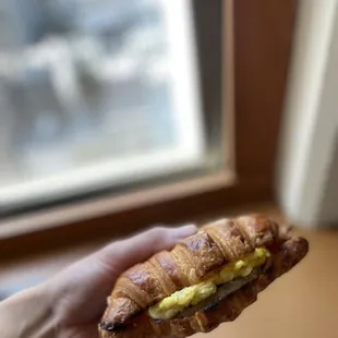 a hand holding a croissant sandwich