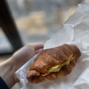 a person holding a croissant sandwich