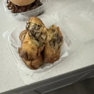 Huge portion of cheesesteak egg rolls up front, crispy bacon burger in the back