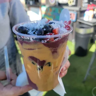 a person holding a cup of fruit and ice cream