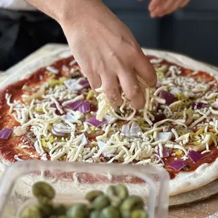 a person putting cheese on a pizza