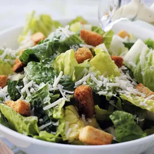 a bowl of salad with croutons and parmesan cheese
