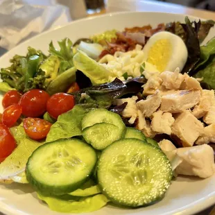 a plate of salad with chicken, tomatoes, cucumbers, and hard boiled eggs