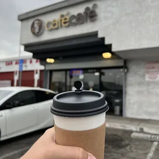 a hand holding a coffee cup in front of a coffee shop