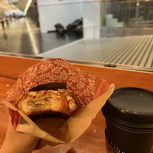 a hand holding a pastry and a cup of coffee