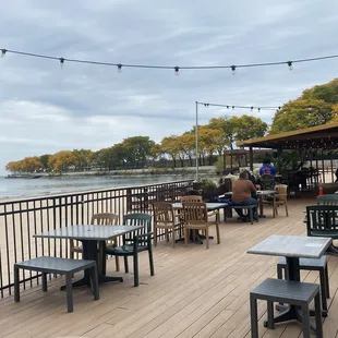 people sitting at tables on a deck overlooking the water