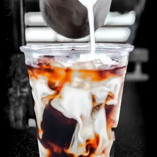 milk being poured into a cup of iced coffee