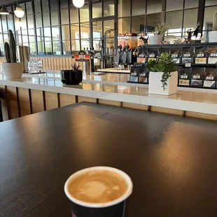 View of part of the coffee bar in the back and a cortado in the front.