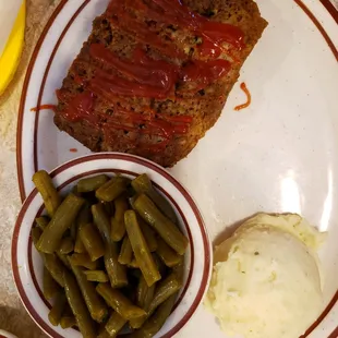 a plate of meatloaf, green beans, and mashed potatoes