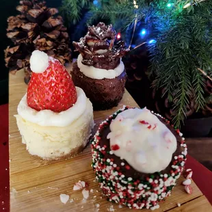 Mini cheesecakes, winter themed. Chocolate with pinecone, vanilla bean with Santa hat and peppermint bark.