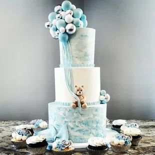 a blue and white cake with a teddy bear on top
