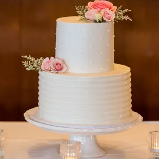 a white wedding cake with pink roses on top