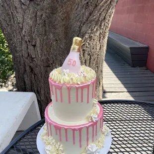 a pink and white cake with a bottle of champagne on top